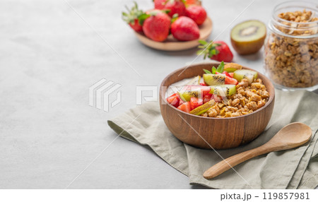 Natural yogurt with granola, kiwi and strawberries in a wooden bowl on a light background  119857981