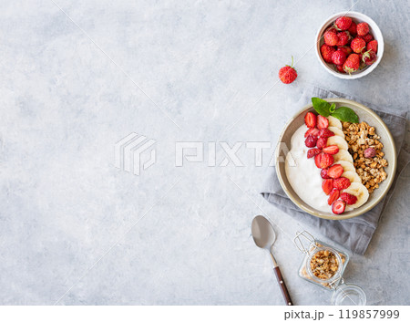 Flat lay of natural yogurt with granola, strawberry and banana in a bowl on a light background Flat lay of natural yogurt with granola, strawberry and banana in a bowl on a light background 119857999