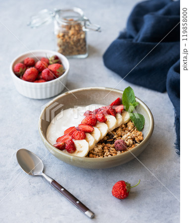 Natural greek yogurt with granola, strawberry and banana in a bowl on a blue background Natural greek yogurt with granola, strawberry and banana in a bowl on a blue background 119858000