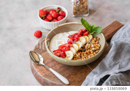 Greek yogurt with muesli, strawberry and banana in a bowl on a wooden board on a light background Greek yogurt with muesli, strawberry and banana in a bowl on a wooden board on a light background 119858069
