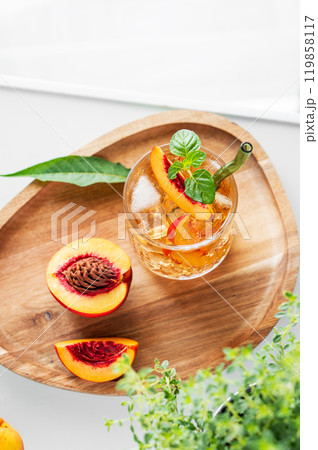 Peach lemonade with ice and mint on a wooden board on a white table. Fresh iced tea in a glass  119858117