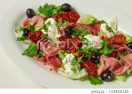 salad with dried tomatoes, prosciutto, soft cheese, olives, homemade, top view, 119858189