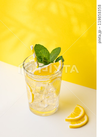 A glass of cold lemonade with lemon, mint and ice on a yellow and white background A glass of cold lemonade with lemon, mint and ice on a yellow and white background 119858358
