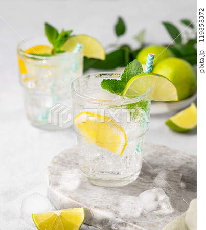 Two glasses of mojito cocktail or tonic with lemon, lime, mint and ice on a marble board. Two glasses of mojito cocktail or tonic with lemon, lime, mint and ice on a marble board. 119858372