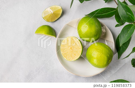 Fresh juicy limes in a plate on a light background with leaves and citrus pieces. Fresh juicy limes in a plate on a light background with leaves and citrus pieces. 119858373