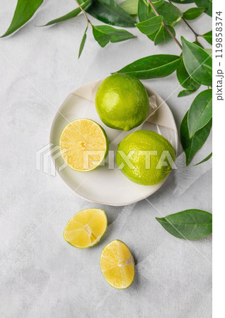 Fresh juicy limes in a plate on a light background with leaves and citrus pieces. 119858374