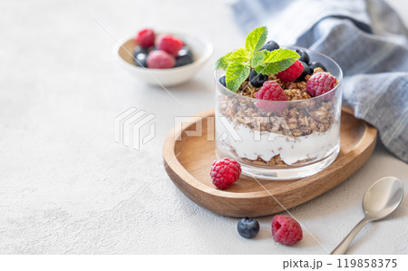 Natural yogurt with granola, raspberries and blueberries in a glass on a wooden board Natural yogurt with granola, raspberries and blueberries in a glass on a wooden board 119858375