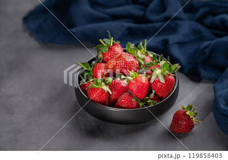 Ripe strawberries in a black bowl on a dark background with a napkin and shadows. 119858403