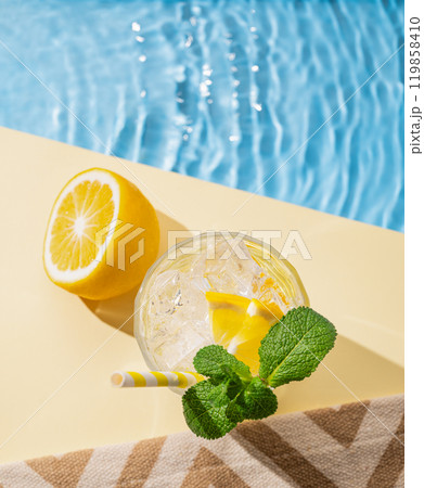 Cold lemonade in a glass with lemon, mint and ice on a yellow background with the edge of a pool Cold lemonade in a glass with lemon, mint and ice on a yellow background with the edge of a pool 119858410
