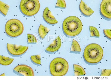 Pattern of juicy slices of kiwi fruits and seeds on a blue background with shadow. 119858430