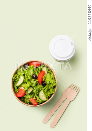 Fresh salad in eco-friendly container with wooden fork and cup on a green background. 119858440