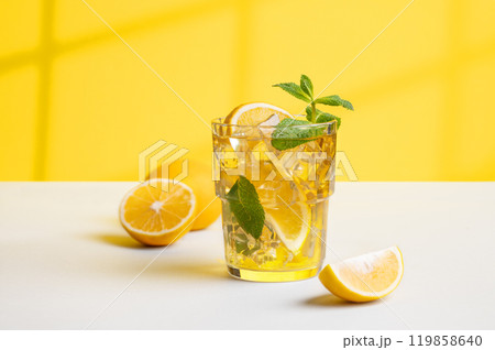 A glass of iced tea with lemon and mint on a yellow and white background with a shadow A glass of iced tea with lemon and mint on a yellow and white background with a shadow 119858640