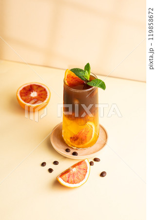 Americano coffee with orange juice (bumble) in a tall glass with ice and mint on a yellow background Americano coffee with orange juice (bumble) in a tall glass with ice and mint on a yellow background 119858672