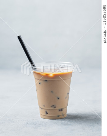 Iced coffee in a recyclable plastic glass with milk and ice on a light background. Iced coffee in a recyclable plastic glass with milk and ice on a light background. 119858699