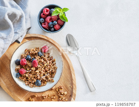 Muesli or granola, raspberries and blueberries in a bowl on a wooden board on a light background Muesli or granola, raspberries and blueberries in a bowl on a wooden board on a light background 119858707