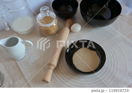 Baking ingredients for baking sweet buns, yeast in black bowl dishes with rolling pin on a table 119858729