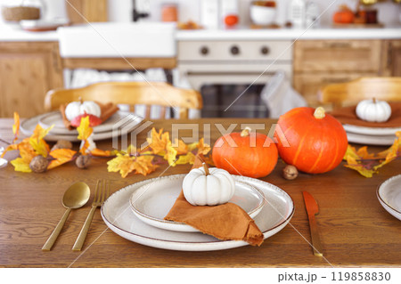 Dinning table setting for fall dinner, with pumpkins, leaves, and candle on kitchen background Dinning table setting for fall dinner, with pumpkins, leaves, and candle on kitchen background 119858830