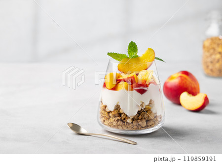 Yogurt parfait with peach and granola in a glass on a light background with fresh fruits.  119859191