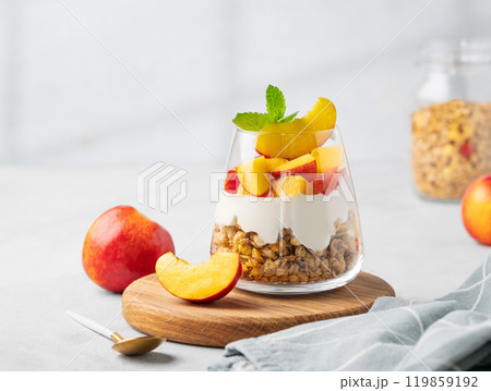 Greek yogurt parfait with peach and muesli in a glass on a wooden board on a light background  Greek yogurt parfait with peach and muesli in a glass on a wooden board on a light background  119859192