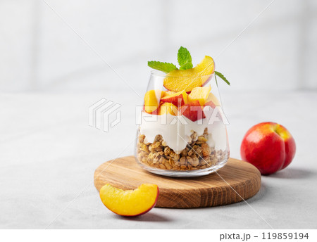 Yogurt parfait with peach and granola in a glass on a wooden board on a light background  119859194