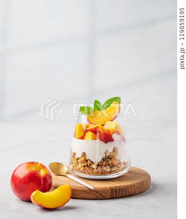 Yogurt parfait with peach and muesli in a glass on a wooden board on a light background  119859195