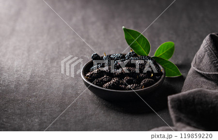 Fresh black mulberry with leaf in black wooden bowl on dark background with napkin. 119859220