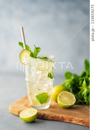 Mojito cocktail in a tall glass with lime, mint and ice on a wooden board on a blue background. Mojito cocktail in a tall glass with lime, mint and ice on a wooden board on a blue background. 119859275