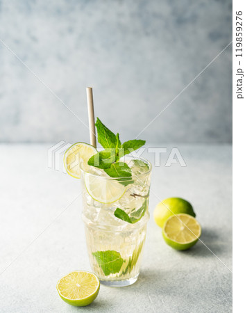 Mojito cocktail in a tall glass with lime, mint and ice on a light textured background. Mojito cocktail in a tall glass with lime, mint and ice on a light textured background. 119859276