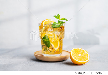 Iced tea with lemon, mint in a glass on light background with shadow and citrus fruits. Iced tea with lemon, mint in a glass on light background with shadow and citrus fruits. 119859662