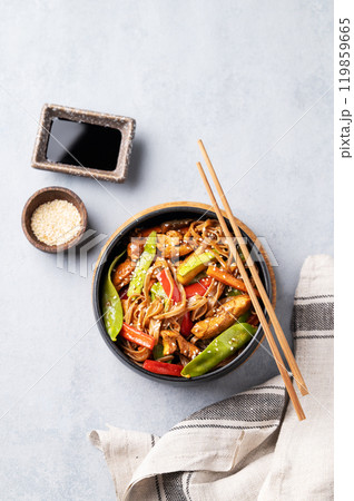 Stir-fry with soba noodles, meat and vegetables on a light background with chopsticks, soy sauce 119859665