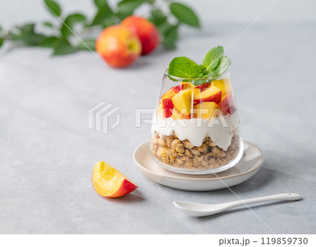 Yogurt parfait with peach and granola in a glass on a light background with fresh fruits.  Yogurt parfait with peach and granola in a glass on a light background with fresh fruits.  119859730