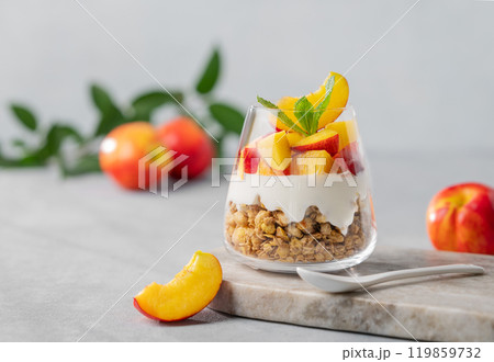 Greek yogurt parfait with peach and granola in a glass on a marble board on a light background Greek yogurt parfait with peach and granola in a glass on a marble board on a light background 119859732