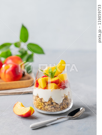 Yogurt parfait with peach and granola in a glass on a light background with fresh fruits. Yogurt parfait with peach and granola in a glass on a light background with fresh fruits. 119859733