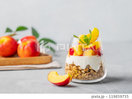 Greek yogurt parfait with peach and granola in a glass on a light background Greek yogurt parfait with peach and granola in a glass on a light background 119859735