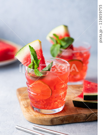 Two glasses watermelon cocktail with lime, ice and mint on a wooden board on a light background  119859755