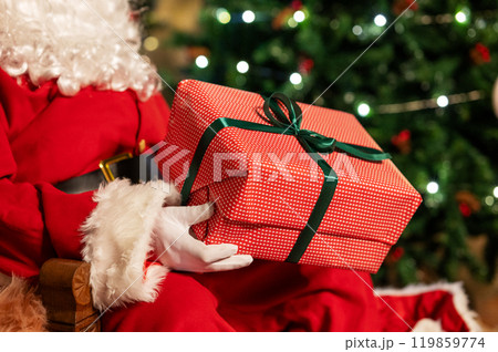 Festive image of Santa Claus in red suit with white beard holding red gift box with green ribbon Festive image of Santa Claus in red suit with white beard holding red gift box with green ribbon 119859774
