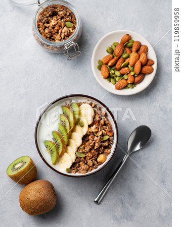 Flat lay of granola with yogurt, banana and kiwi in a bowl on a light background. 119859958