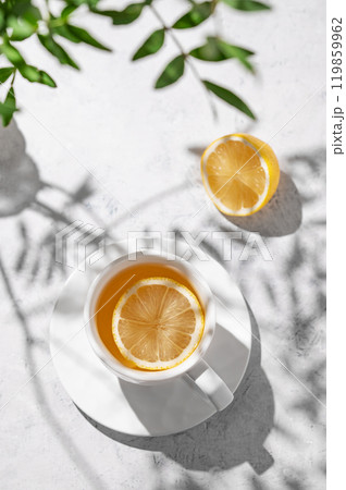 A cup of tea with lemon and green branch on a white table. Breakfast detox and healthy concept. A cup of tea with lemon and green branch on a white table. Breakfast detox and healthy concept. 119859962