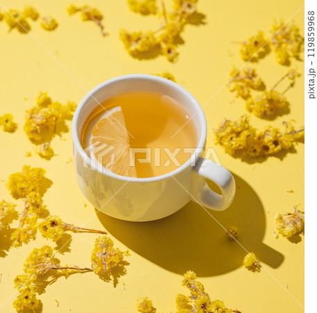 Herbal tea with immortelle and lemon in a white cup on a yellow background close up. 119859968