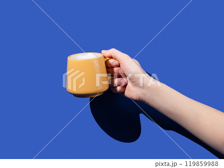 Hand hold yellow cup coffee on a blue background. Design concept for breakfast pastry mockup  119859988