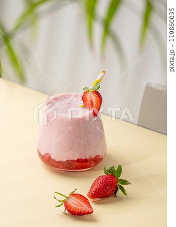 A strawberry milkshake or smoothie in glass with strawberries on a yellow background 119860035