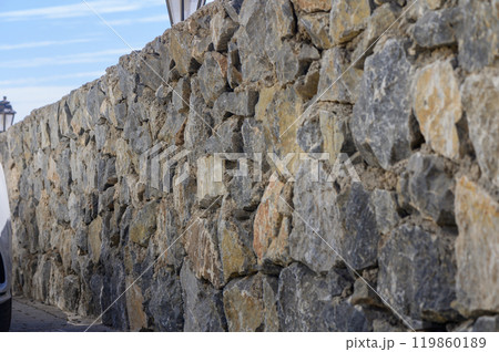 A weathered stone wall stretches along a quaint pathway under a clear blue sky, showcasing the beauty of natural materials in architecture 119860189