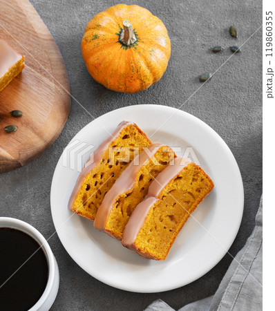 Pumpkin sweet bread or cake with icing on a plate on a dark background with decorative pumpkins 119860355