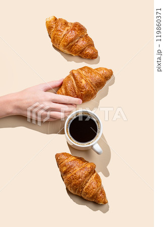 Hand holding fresh croissant on yellow background with shadow and cup of espresso coffee. Hand holding fresh croissant on yellow background with shadow and cup of espresso coffee. 119860371