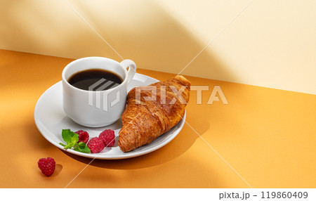 Cup of coffee and fresh croissant with raspberries on a white plate on an yellow background Cup of coffee and fresh croissant with raspberries on a white plate on an yellow background 119860409