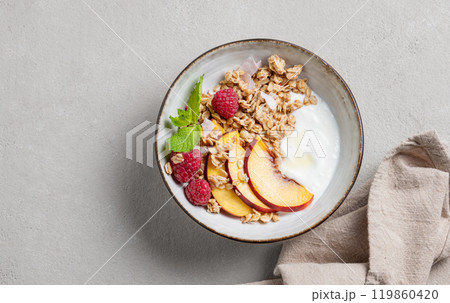 Greek natural yogurt with oat granola or muesli, peach, raspberry and mint in a bowl Greek natural yogurt with oat granola or muesli, peach, raspberry and mint in a bowl 119860420