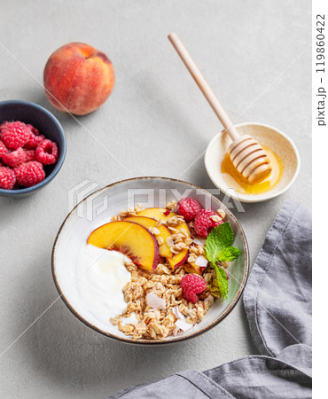 Greek natural yogurt with oat granola or muesli, peach, raspberry and honey in a bowl  119860422