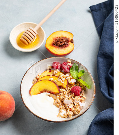 Greek natural yogurt with oat granola or muesli, peach, raspberry and honey in a bowl  119860425