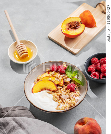 Natural yogurt with oat granola, peach, raspberry and honey in a bowl on a blue background Natural yogurt with oat granola, peach, raspberry and honey in a bowl on a blue background 119860427