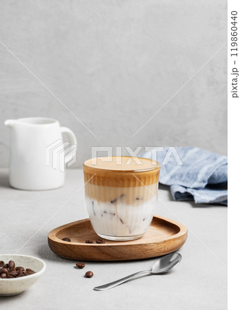Dalgona coffee. Whipped instant coffee in a glass with ice on a wooden board on a gray background Dalgona coffee. Whipped instant coffee in a glass with ice on a wooden board on a gray background 119860440